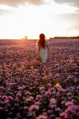 Fototapeta na wymiar Beautiful young woman in a straw hat on a phacelia flower field at sunset