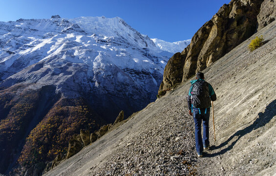 A male hiker walking along a narrow high-altitude trekking trail toward Tilicho Lake in the Annapurna region of Nepal.
