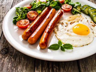 Breakfast - sunny side up egg, fried sausages and vegetables served on wooden table
