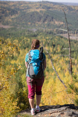 Red-haired girl standing with a backpack on a rock on a background of autumn forest