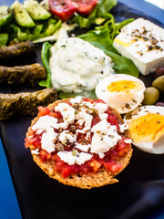 Crete plate - fresh Greek salad, feta cheese, dolmades, tomatoes, lettuce, boiled egg, black and green olives on black plate