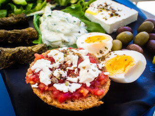 Crete plate - fresh Greek salad, feta cheese, dolmades, tomatoes, lettuce, boiled egg, black and green olives on black plate