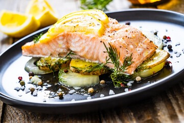 Roasted salmon steak with lemon and onion served on black plate on wooden table
