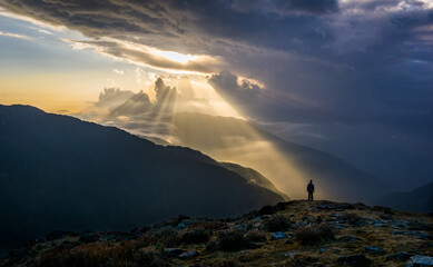 A conceptual image of a man being hopeful, positive and optimistic. A person looking at a beam of sun rays in a dark and moody atmosphere. Sunset in Langtang National Park, Nepal on Gosainkunda trail.