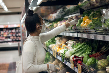 Young Asian women wearing face mask and hand in rubber gloves choosing fruits and vegetables at farmer's market.