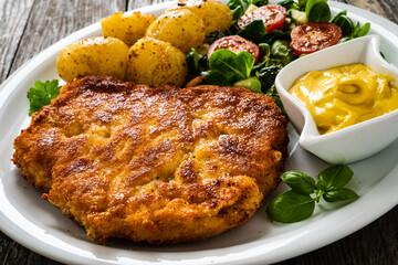 Breaded pork chop with boiled potatoes and vegetable salad on wooden background
