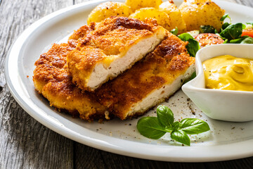 Breaded pork chop with boiled potatoes and vegetable salad on wooden background
