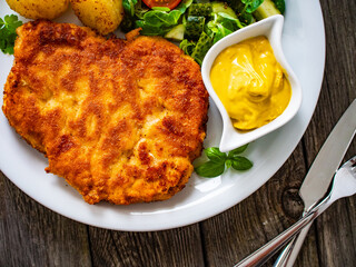 Breaded pork chop with boiled potatoes and vegetable salad on wooden background
