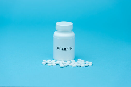 Treatments for Coronavirus (COVID-19): IVERMECTIN in white bottle packaging with scattered pills. Isolated on blue background.