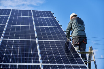 Back view of man technician standing on ladder and installing photovoltaic solar panel. Male worker...
