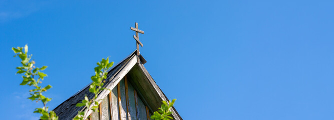 Christian cross on the roof of the house against the blue sky. Symbol of faith for copy space.