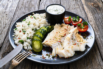Fish dish - fried cod fillet with basmati rice and vegetables on wooden table
