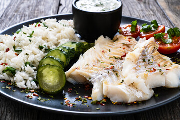Fish dish - fried cod fillet with basmati rice and vegetables on wooden table
