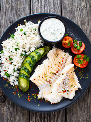 Fish dish - fried cod fillet with basmati rice and vegetables on wooden table
