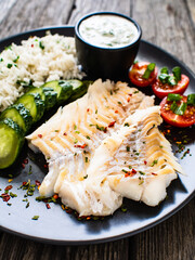 Fish dish - fried cod fillet with basmati rice and vegetables on wooden table
