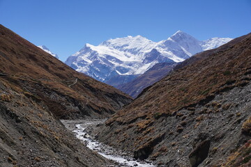 Small tributary of Marshyangdi river near Yak Kharka in Manang with view of Annapurna mountain peak at a distance.  Trail to Thorong La on Annapurna Circuit Trek Nepal.