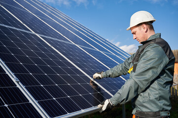 Side view of man technician in safety helmet repairing photovoltaic solar module. Professional...