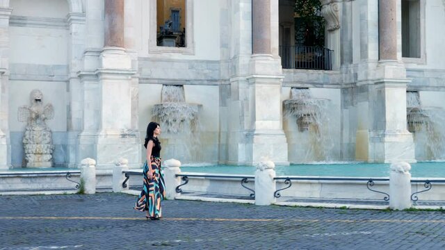 young elegant woman walking in the city with the fountain in the background