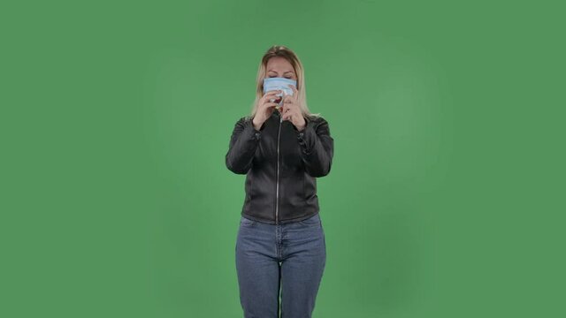 Portrait of beautiful young woman in medical protective face mask looking at camera and applying antiseptic on her hands in order to prevent the spread of coronavirus. Blonde with loose hair in a