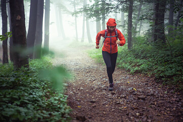 Female outdoor runner, running through misty forest on a rainy day.