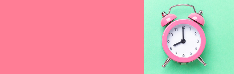 Pink alarm clock on two tone color pink and mint background. Top view, place for text. Horizontal banner