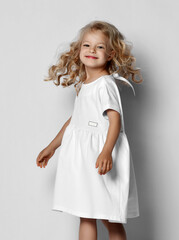 Little blonde curly positive princess girl in white casual dress and sneakers standing walking with...