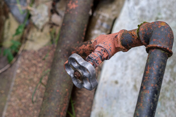 An old rusty plumbing valve is installed in a metal pipe and is located outside against the background of a concrete slab.
