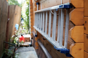 A metal construction ladder made of aluminum profiles hangs on a wooden wall.