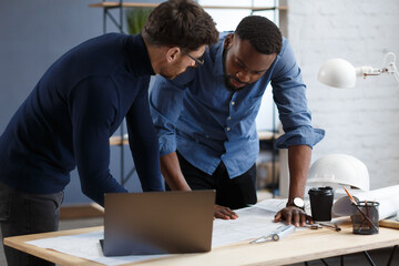 Multiracial engineer team working in office with blue prints and architect equipment...