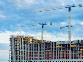 Multi-story residential building is being constructed using a crane. View of a large construction site in the city. Concept - sale of tower cranes. Erection of building on the background of the sky.