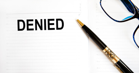 In the notebook is the inscription DENIED, next to the pen pointing to the word, glasses and graphics.