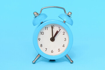Blue alarm clock on blue background close up. 1 a.m., 1 p.m. Time concept.