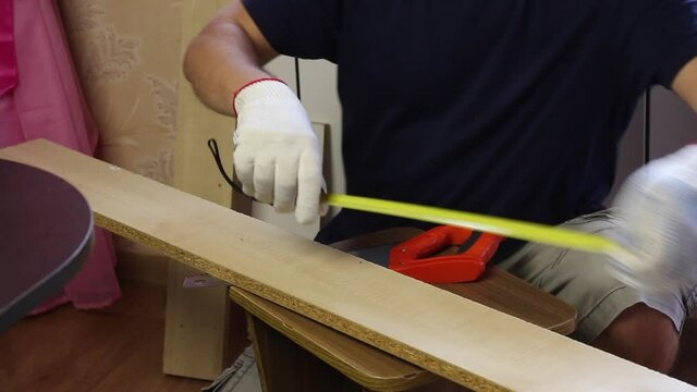 A man measures a board with a tape measure. Making furniture at home.