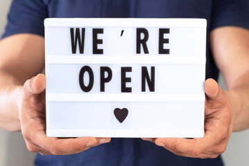 End of quarantine. Man holding lightbox with greeting text message We're open in his hands. Hotel, cafe, local shop, service owner welcoming guests after coronavirus outbreak and people shutdown.