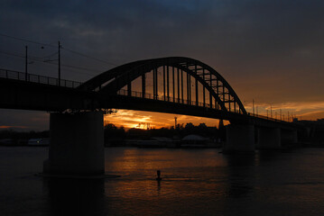 The Old Sava Bridge at sunset in Belgrade, Serbia. The bridge crosses the Sava River in central Belgrade. The bridge is silhouetted against the orange glow of the sunset.
