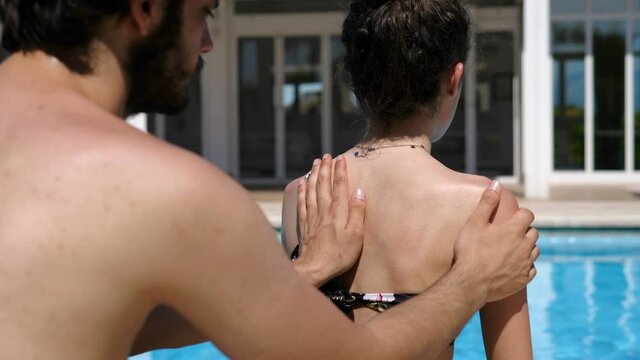 Holiday, summer - young man spreading sunscreen on his girlfriend's shoulders