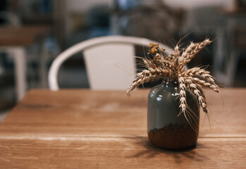 Hygge home decor concept. Small ceramic vase with dried wheat spikes standing on the table. Toned shot with copy space