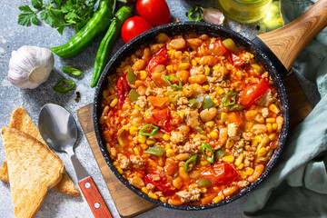 Traditional mexican food. Chili con carne from meat, beans and vegetables on dark stone table.