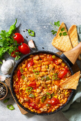 Traditional mexican food. Chili con carne from meat, beans and vegetables on dark stone table. Top view flat lay background. Copy space.