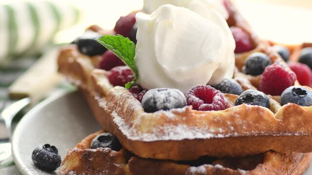 Belgian waffles on plate with ice cream and berries. Sweet waffle breakfast. Dessert served on table with napkin and fork.