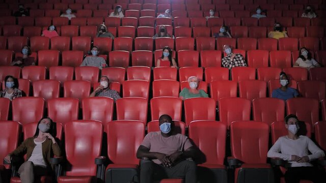 Diverse masked audience keeping social distance while watching comedy movie during coronavirus epidemic. Multi-ethnic viewers in protective masks laughing at movie during covid19 spread