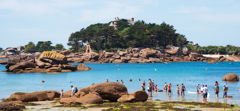 Brittany, France. Unrecognizable people bathing and relaxing at beach with a view of castle at Pink Granite Coast near Ploumanach. Family vacation at Cotes d'Armor background.