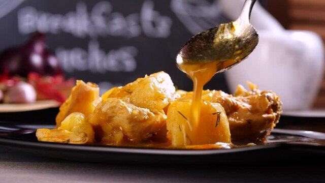 Anonymous person spilling spoon of warm sauce on roasted potato with meat in cafe