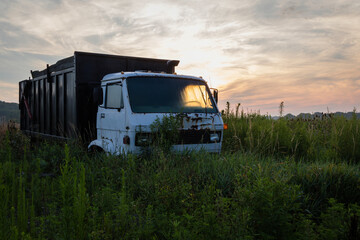 Sunlight relfects through window of old dump truck on grass field at sunrise