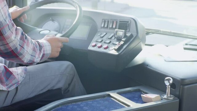 Male bus driver in a plaid shirt, in the summer, rides a bus on the road, collects fellow travelers