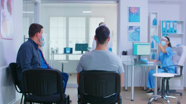 Doctor with face mask against covid 19 inviting patient in examination room. Nurse helping invalid senior woman with walking frame in hospital waiting area.