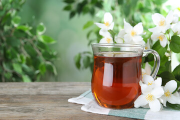 Cup of tea and fresh jasmine flowers on wooden table. Space for text
