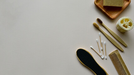 Bamboo toothbrushes, natural soap on a wooden plate, bath loofah and other eco-friendly body care products on a beige paper background. Zero waste concept. View from above. Copy space.