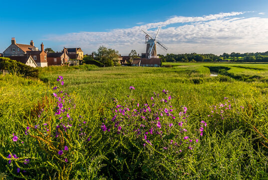 Purple flowers in the foreground of a view of the village of Cley and drainage channels in the marshes in Norfolk, UK
