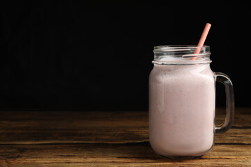 Tasty milk shake with straw in mason jar on wooden table. Space for text